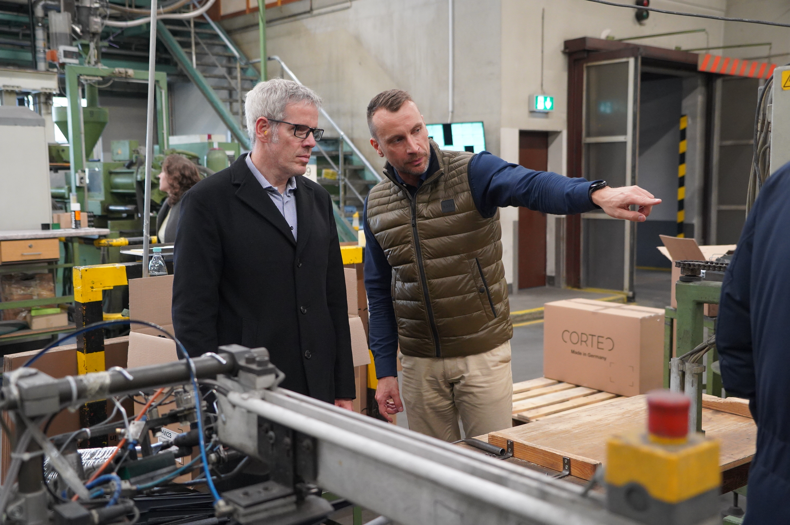 Geschäftsführer Torsten Schmitt (links) zeigt Landrat Christian Engelhardt (rechts) wie die nachhaltigen Kleiderbügel in Wahlen produziert werden.